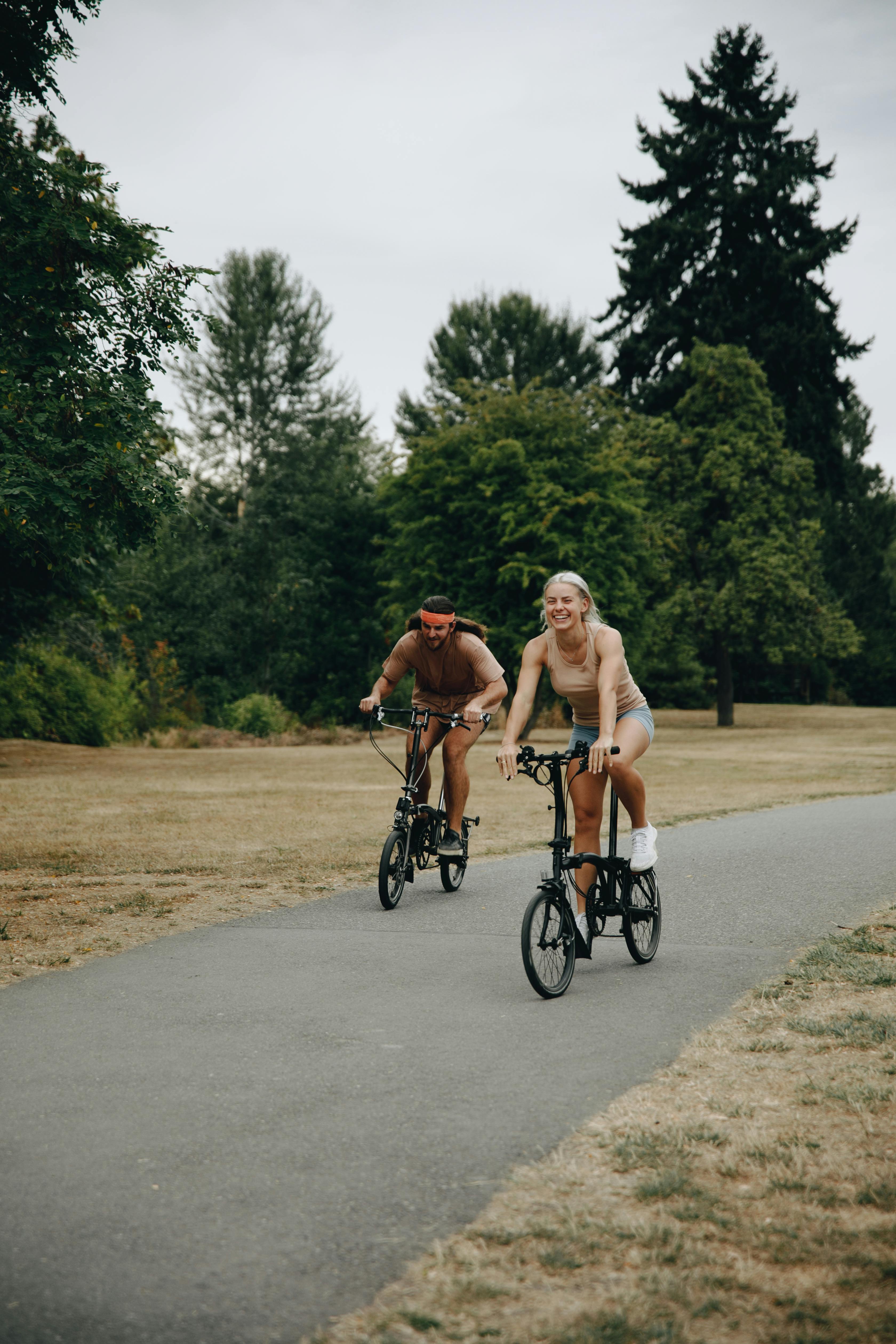 A man and woman cycling together on a park path surrounded by lush trees.