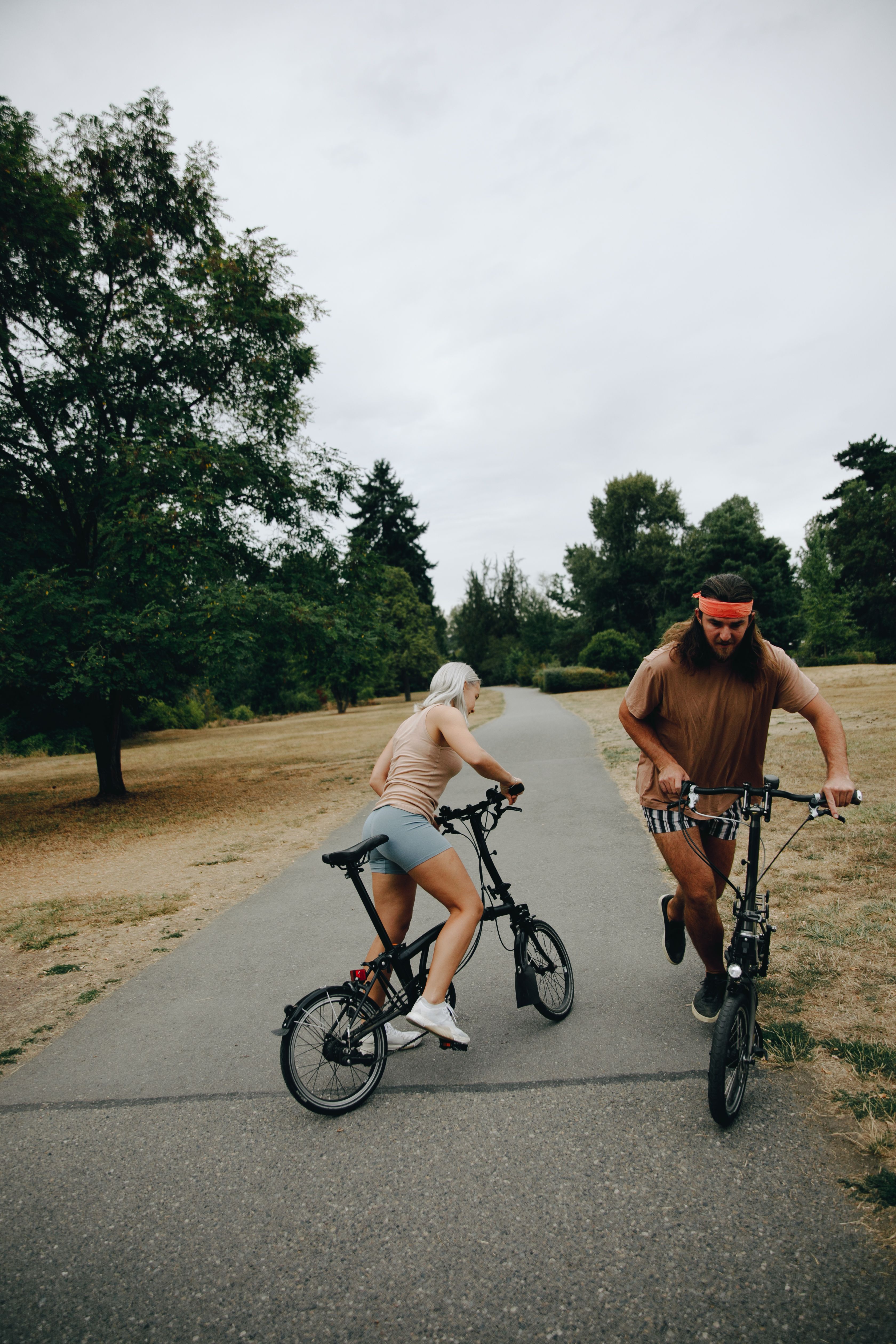 Two adults enjoying a leisure bike ride in a park setting on a cloudy day.