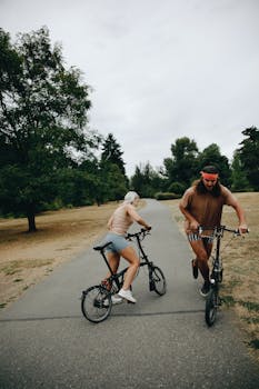 Two adults enjoying a leisure bike ride in a park setting on a cloudy day.