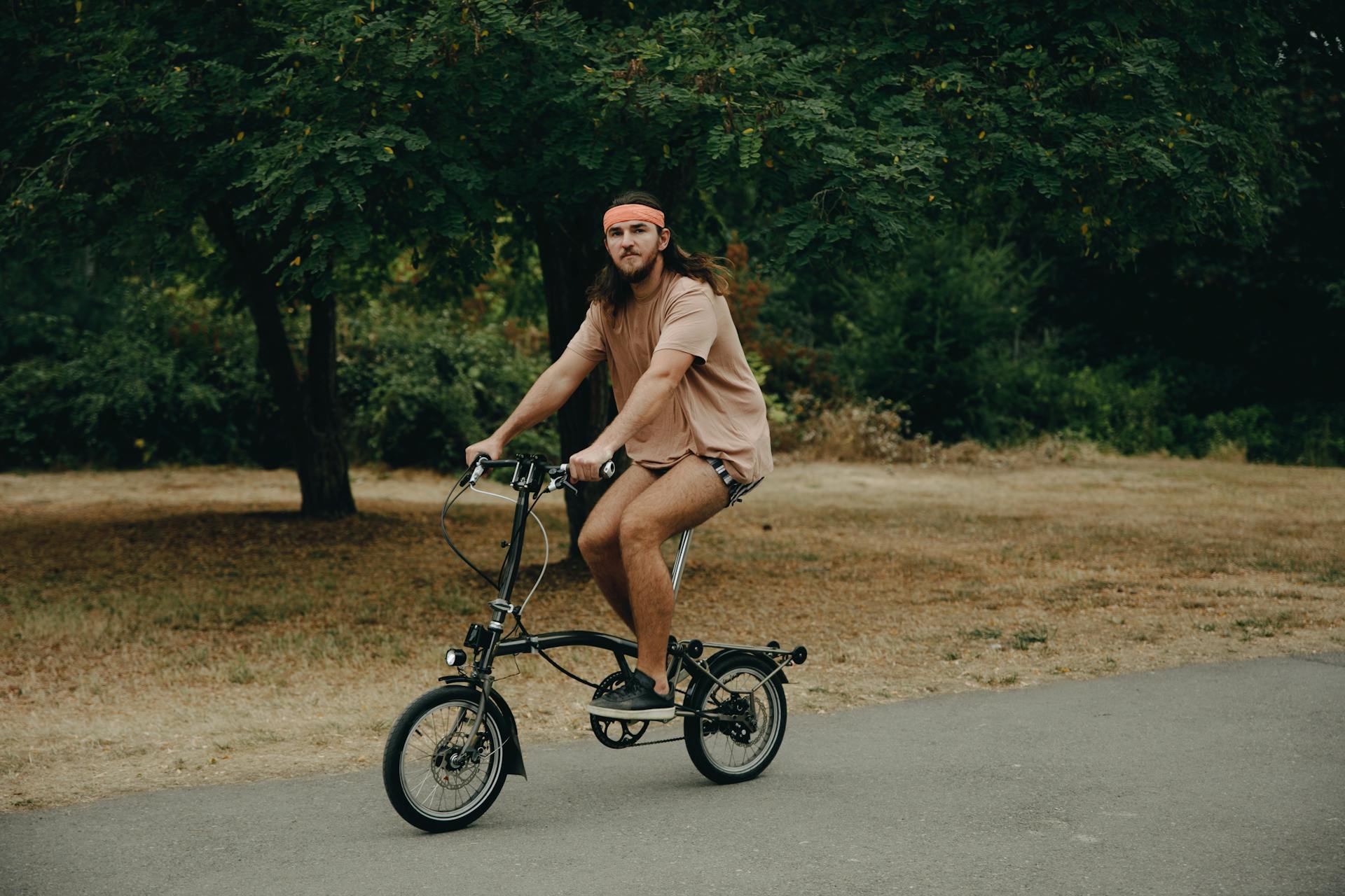 Casually dressed man with long hair biking outdoors in a park.