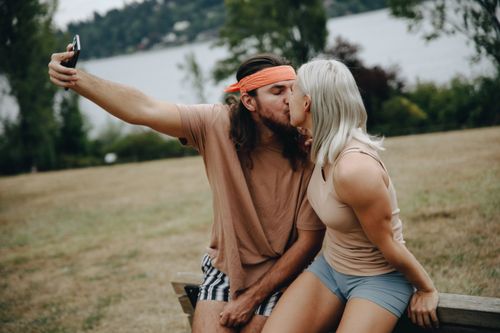 Free A couple sharing a kiss while capturing a selfie outdoors, depicting love and connection. Stock Photo