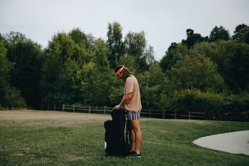 Free Man standing outdoors with a sports bag in a park. Green trees in the background. Stock Photo