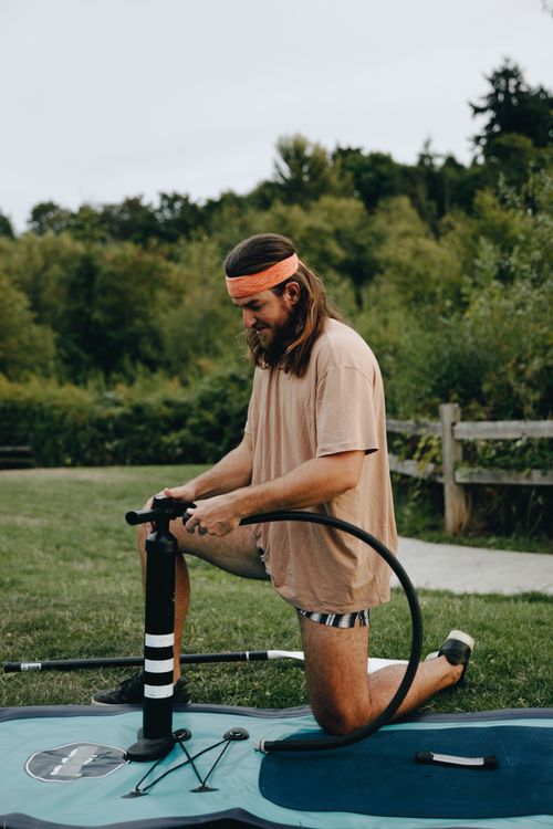 Free Adult male inflating a paddleboard outdoors, showcasing summer leisure activities. Stock Photo