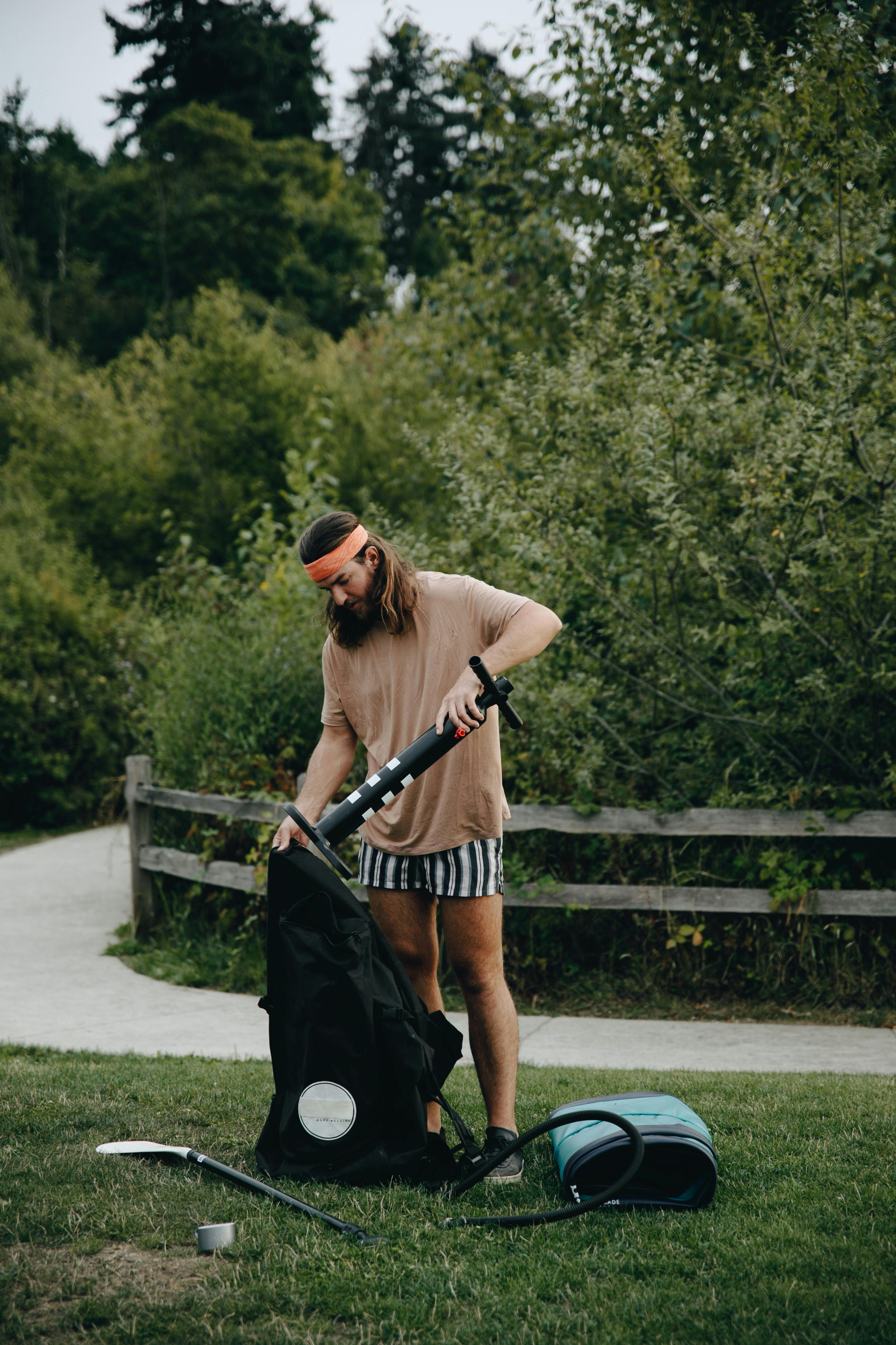 A man pumps an air mattress in a scenic park setting, ideal for camping and outdoor recreation.
