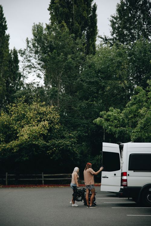 Free Couple loading bicycles into a campervan in a scenic outdoor parking lot, highlighting summer recreation and travel. Stock Photo