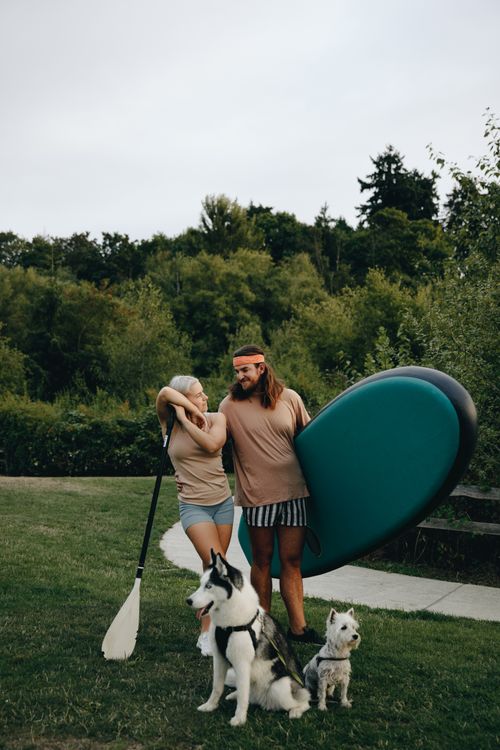Free A couple stands with their dogs and paddleboard outdoors, enjoying a summer day. Stock Photo