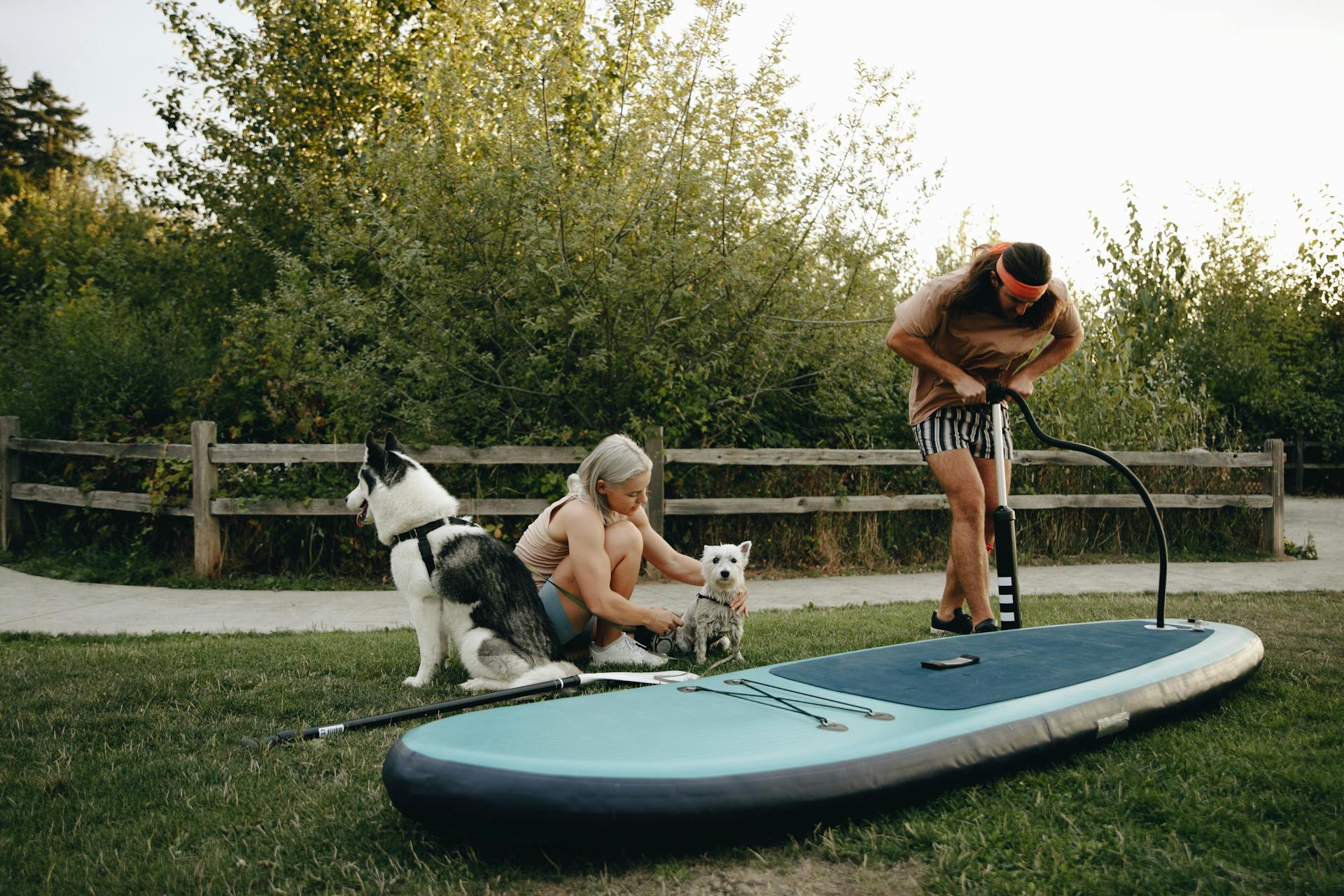 Man Inflating a SUP Board and Woman Sitting next to Him with Dogs