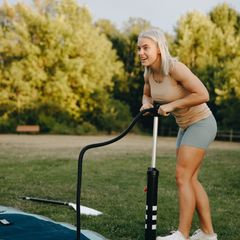 A smiling woman using a black floor pump on the grass