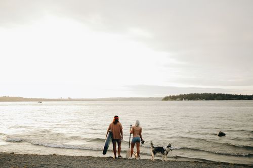 Free Couple with surfboards and dog enjoying a serene day on a sandy beach. Stock Photo