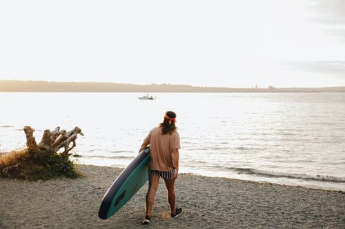 Free A surfer with a board gazes at the waves under the soft morning light at a beach. Stock Photo