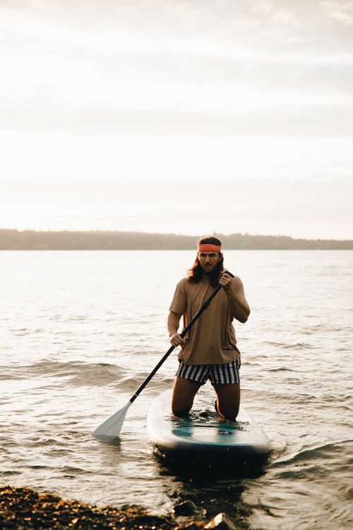 Free A man enjoys paddleboarding during sunset, embodying a serene water activity and outdoor recreation. Stock Photo