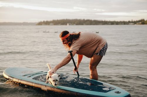 Free A man enjoys paddleboarding with his dog on a calm sea during sunset, capturing a serene moment. Stock Photo