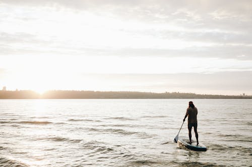 A Back View of a Person Standing on a Sup Board while Holding a Paddle