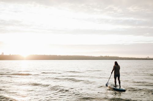 Free A person paddleboarding on the sea during a beautiful sunset, capturing a peaceful vacation moment. Stock Photo