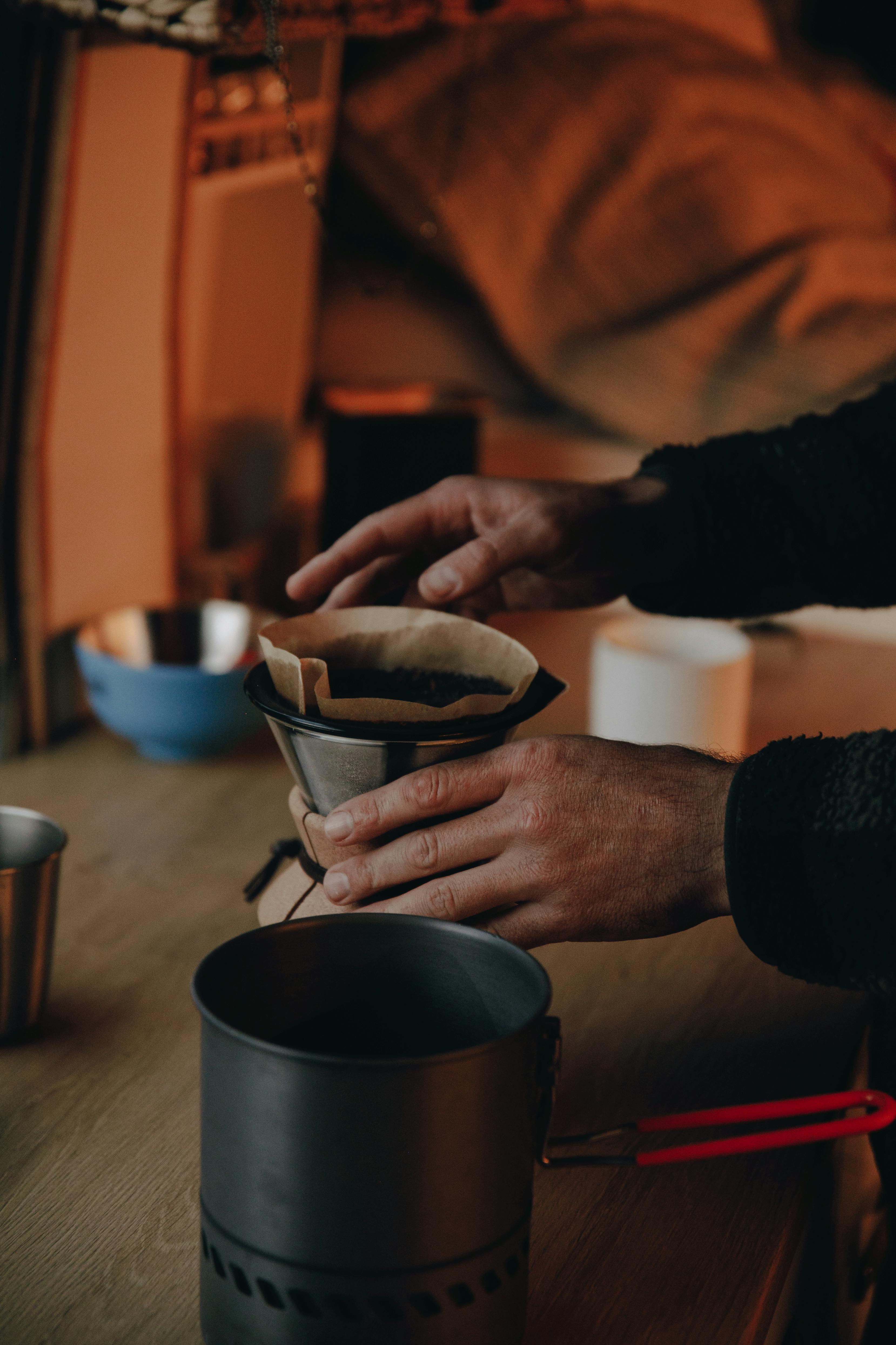 Warm-toned image of hands preparing coffee using a drip filter indoors on a wooden table.