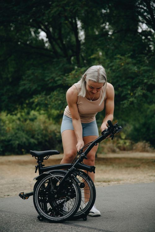 Free Caucasian woman setting up a folding bike outdoors on a sunny day. Stock Photo