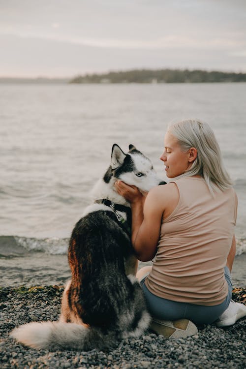 Woman Sitting on the Shore while Looking at Her Dog