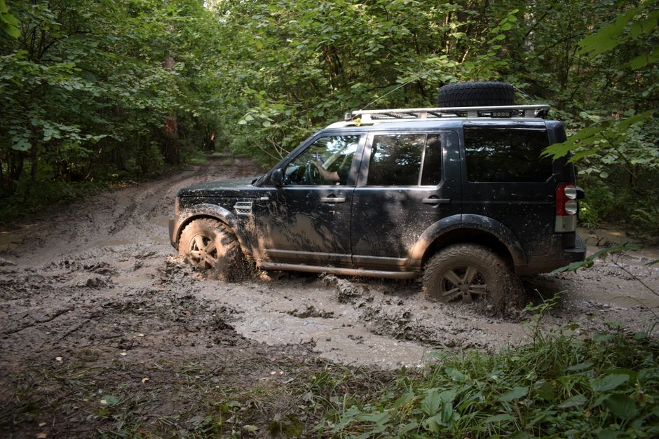 An SUV driving through muddy trails in a dense forest, showcasing off-road capabilities.