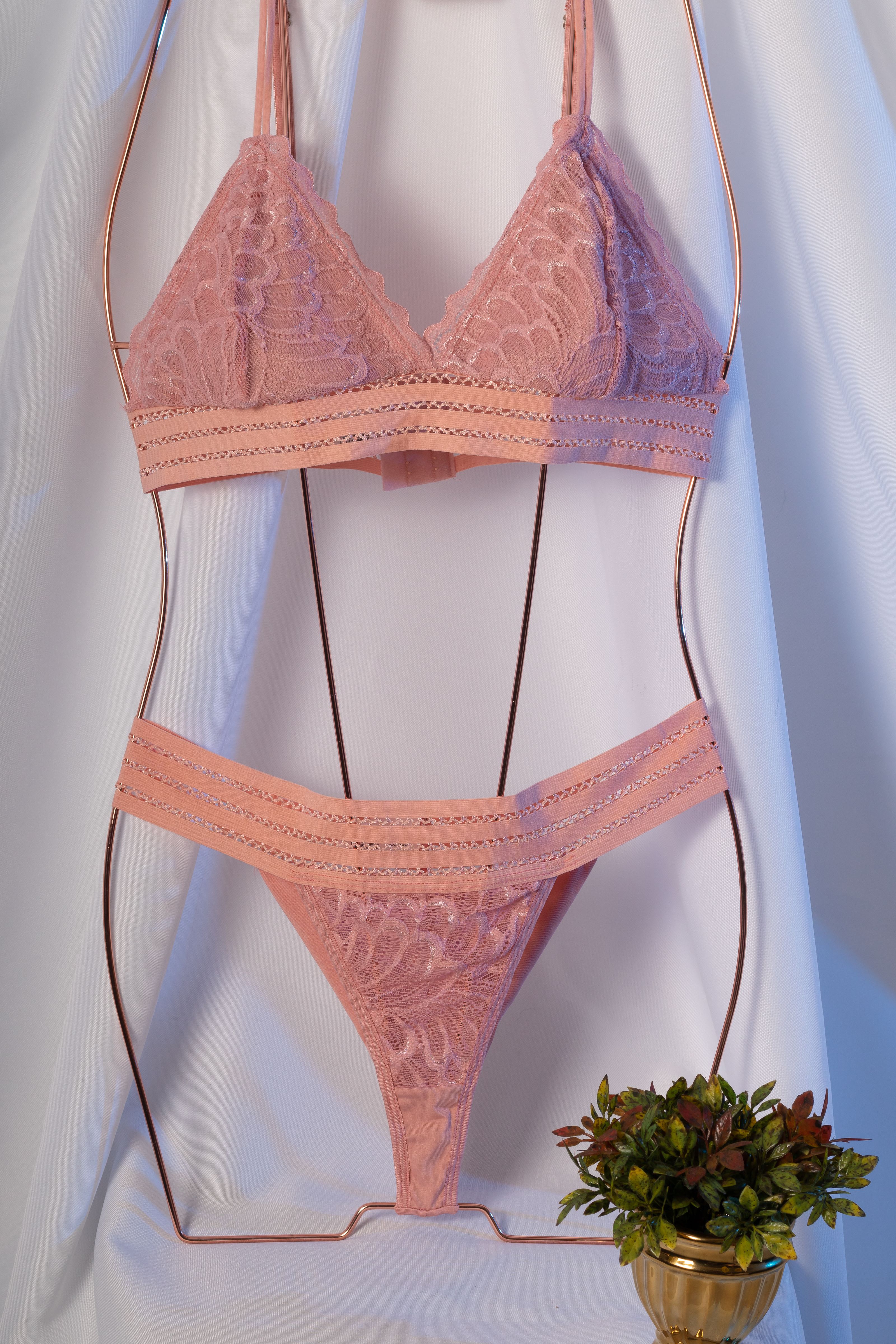 Conjunto de lingerie de renda rosa com sutiã e calcinha em estrutura de metal, estilizado com tecido branco.