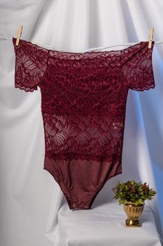 Burgundy lace lingerie hanging on a clothesline with neutral draped background in elegant setup.