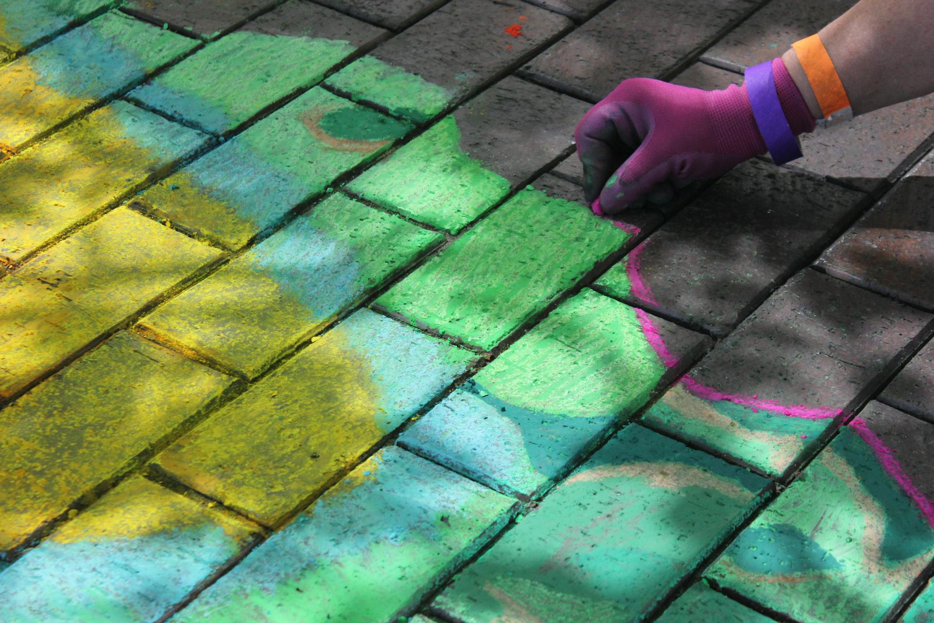 A vibrant chalk drawing on a Kansas City sidewalk with an artist's hand in colorful gloves.