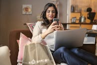 一位女士坐在沙发上，手拿笔记本电脑和智能手机，享受着现代生活的休闲时光