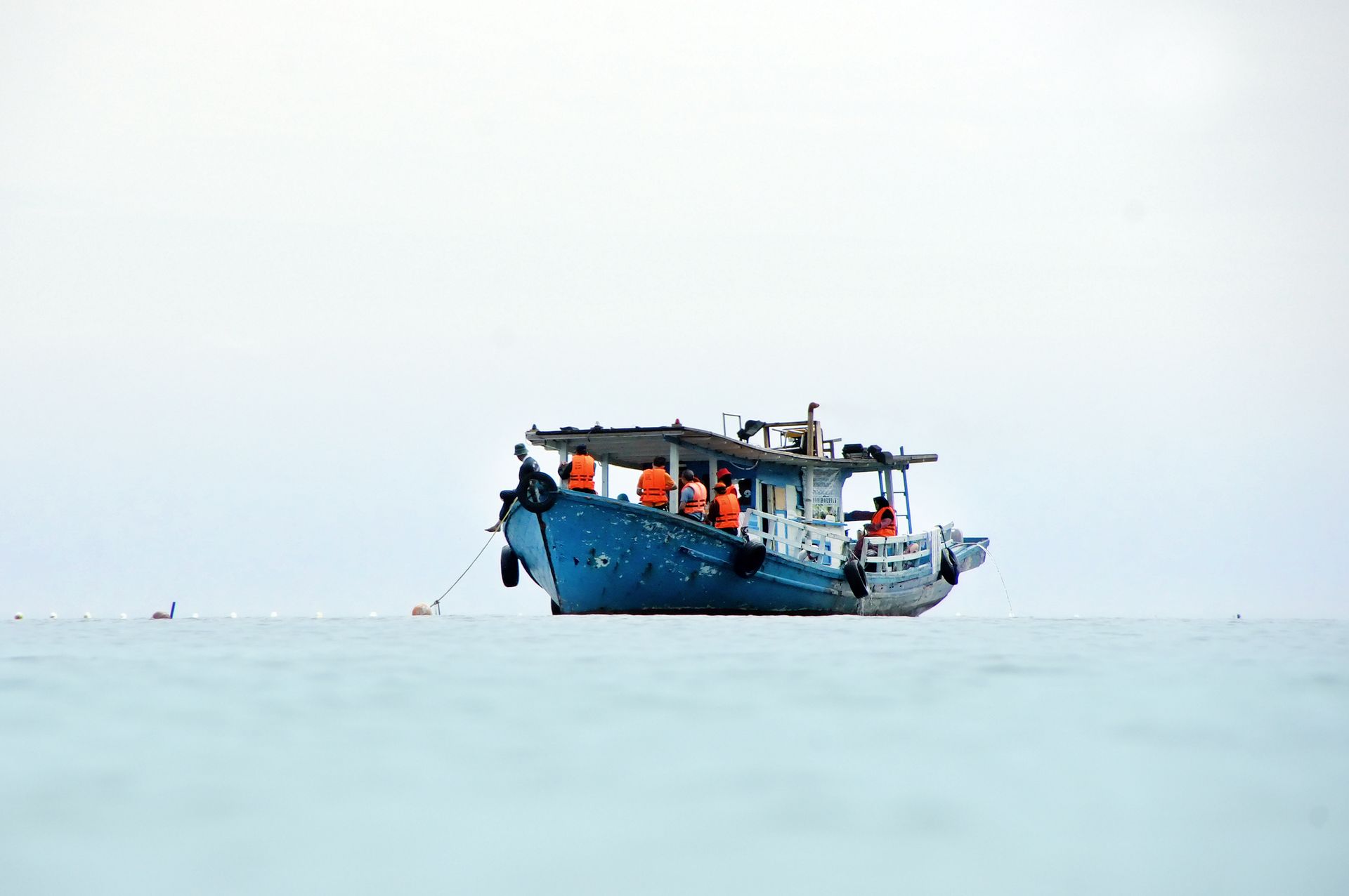 A tranquil blue fishing boat with passengers in life vests on a calm sea under a clear sky.