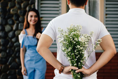 Homem Segurando Uma Flor Com Hálito De Bebê Na Frente De Uma Mulher Em Pé Perto De Uma Parede De Mármore