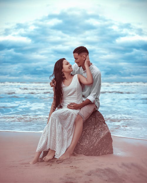 Free A Couple Sitting on a Rock at the Beach Stock Photo