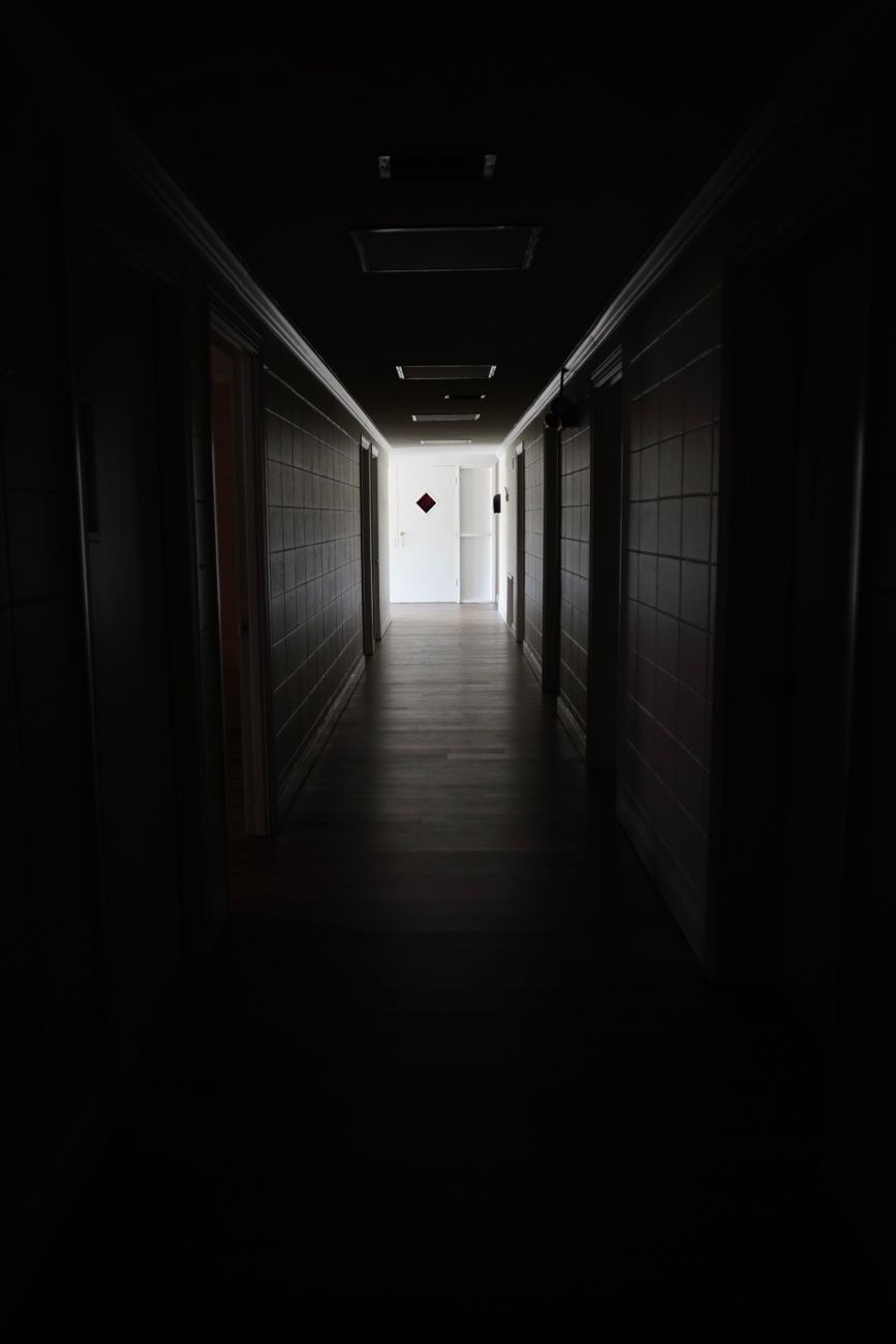 A dark and empty hallway indoors leading to a closed door, creating an eerie atmosphere.. pexels, dark, empty