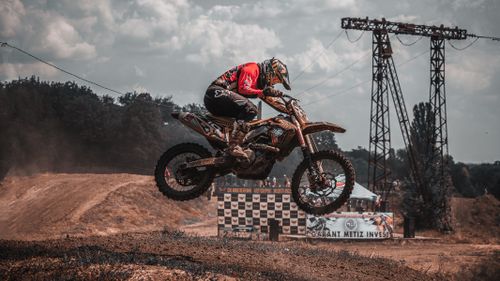 Free Motocross racer jumps high over dusty track during an outdoor event, showcasing extreme sports action. Stock Photo