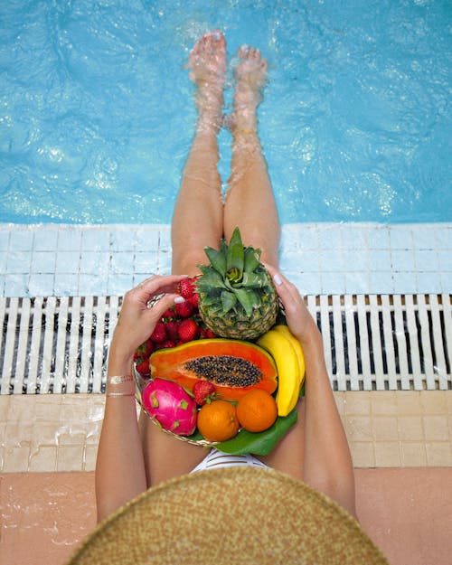 A Woman Holding Various Fruits by the Pool