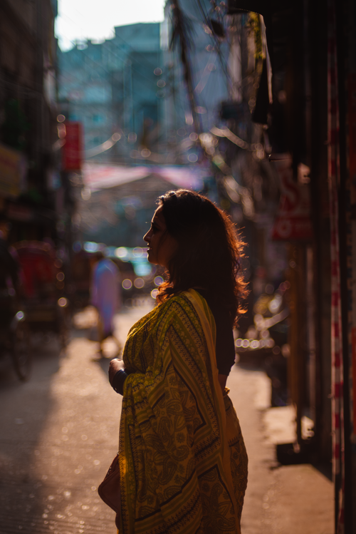 Free A woman in a vibrant sari walks through a sunlit, crowded street, casting an elegant silhouette. Stock Photo