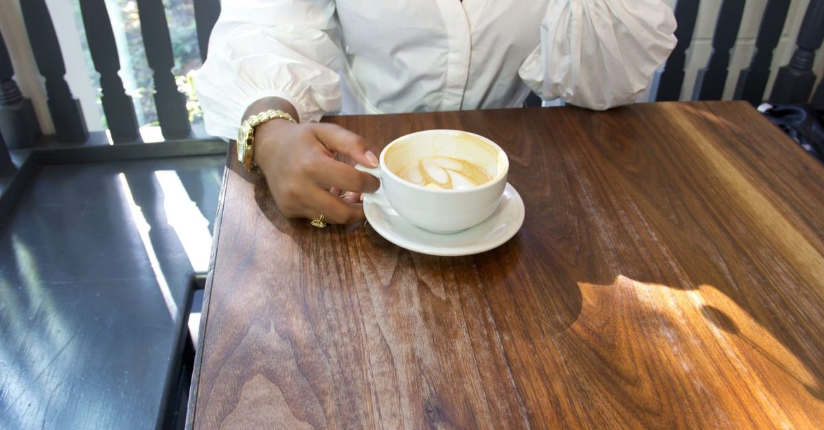 person drinking coffee by window phone face down on table