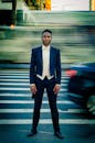 一个穿着燕尾服的男人自信地站在繁忙的城市街道上，过往车辆的运动模糊可见