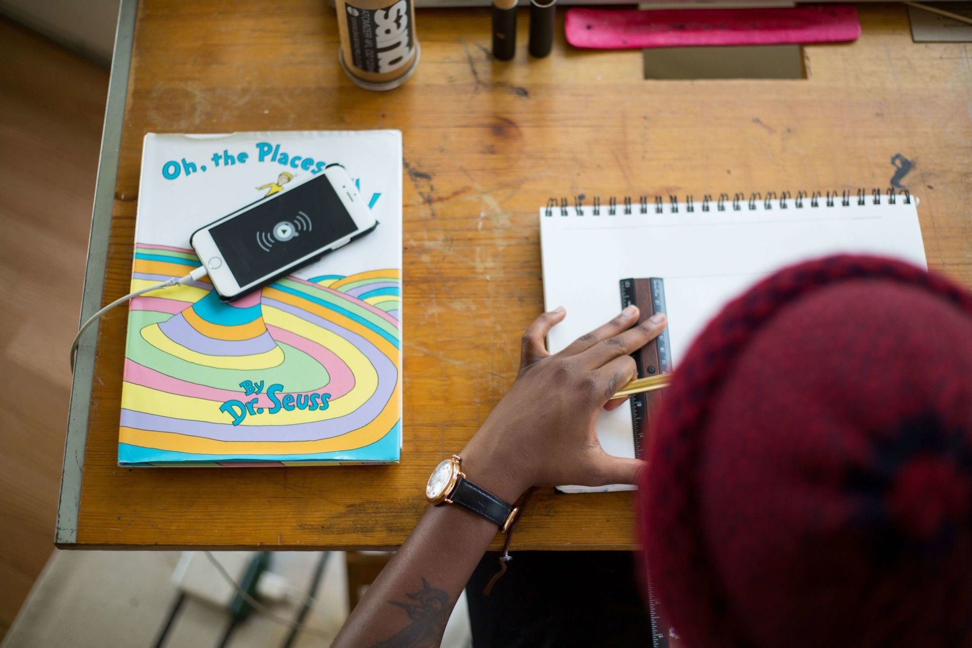 Workspace with drawing, smartphone, and Dr. Seuss book on wooden desk.