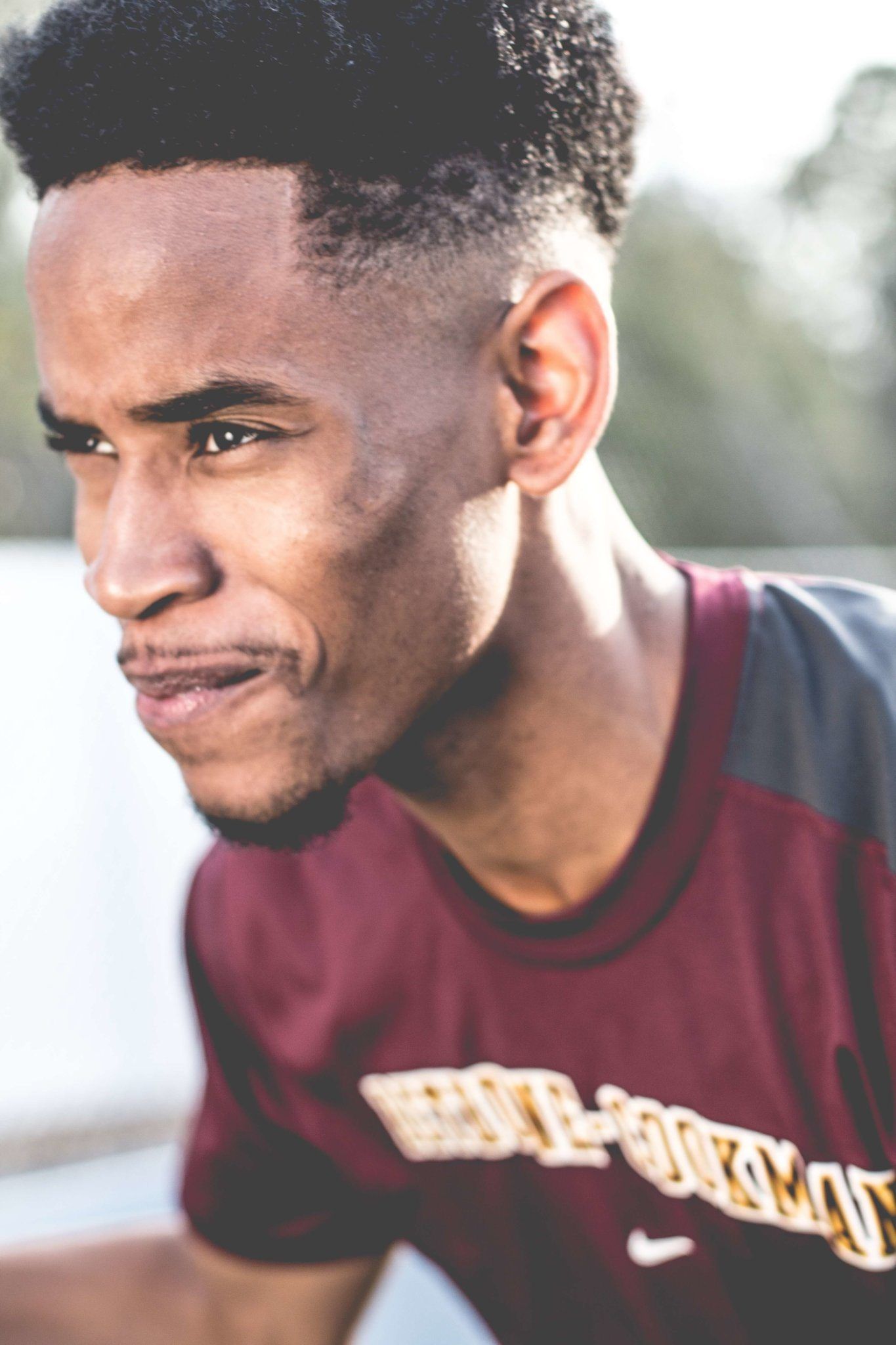 Portrait of a determined young athlete in maroon sportswear outdoors, exuding focus and determination.