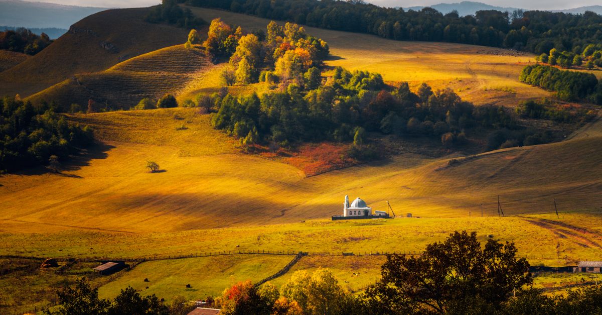 A scenic view of the Volta Region landscape with rolling hills and a church building in the distance, golden hour light