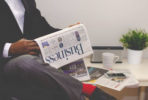 Uomo Che Legge Il Giornale Mentre Era Seduto Vicino Al Tavolo Con Smartphone E Tazza