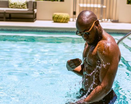 A man wearing sunglasses takes a cool dip in an outdoor swimming pool, enjoying a sunny day.