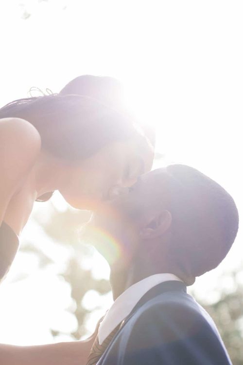 Free A romantic portrait of a couple kissing outdoors, backlit by bright sunlight, creating a dreamy effect. Stock Photo
