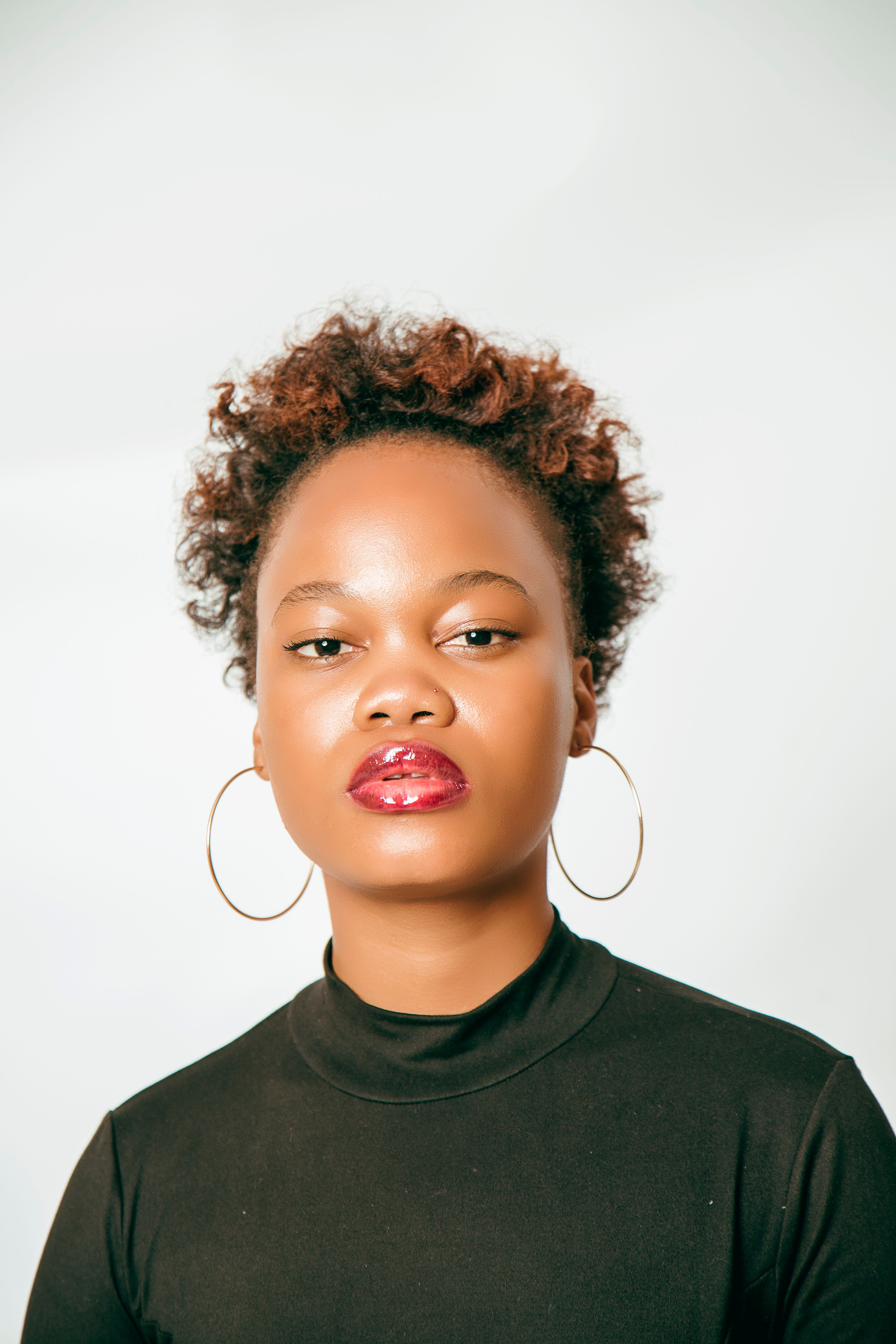 Studio portrait of a stylish woman with curly hair and hoop earrings on a white background.