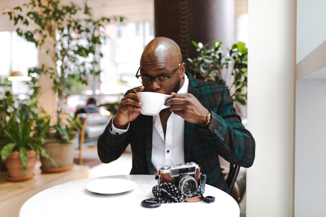 Man Sitting in Front of Round Table While Sipping from White Ceramic Mug