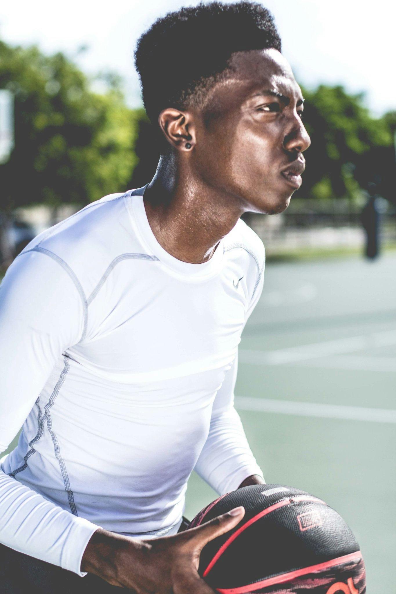 man in white crew neck long sleeved shirt holding black and red basketball