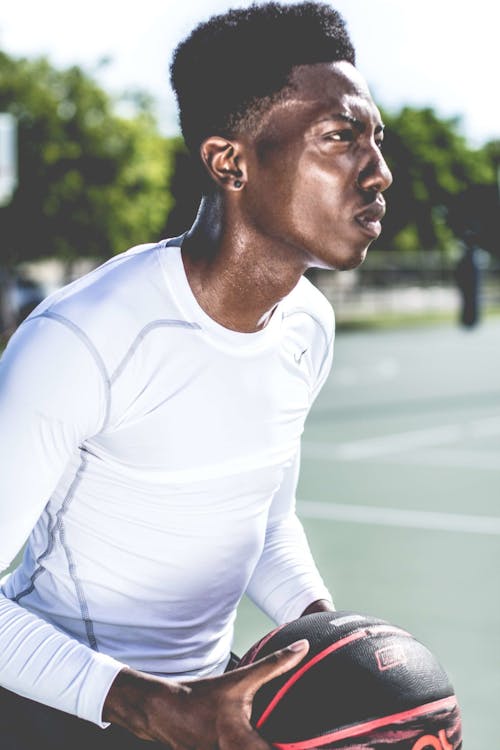 Man in White Crew-neck Long-sleeved Shirt Holding Black and Red Basketball