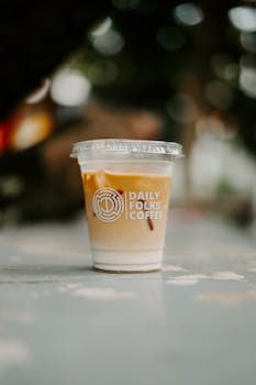 Chilled iced coffee in a branded plastic cup with a lid on a rustic table with blurred background.