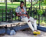 夏天，一个时尚的男人穿着花卉衬衫和破洞牛仔裤，坐在公园的长凳上