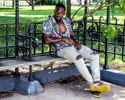 夏天，一个时尚的男人穿着花卉衬衫和破洞牛仔裤，坐在公园的长凳上