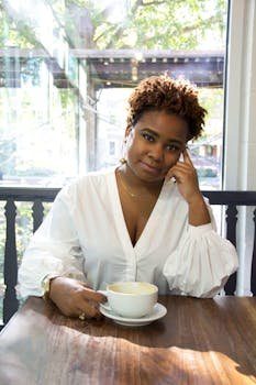 一位身穿白色衬衫的女子面带微笑，在明亮的咖啡馆里享用咖啡