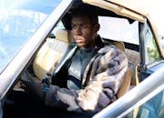 在一个晴朗的日子，一个穿着时髦皮大衣的人驾驶着一辆老式汽车